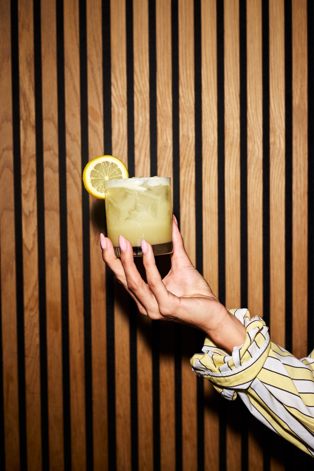 A lemon-garnished cocktail held against the wood-lined bar