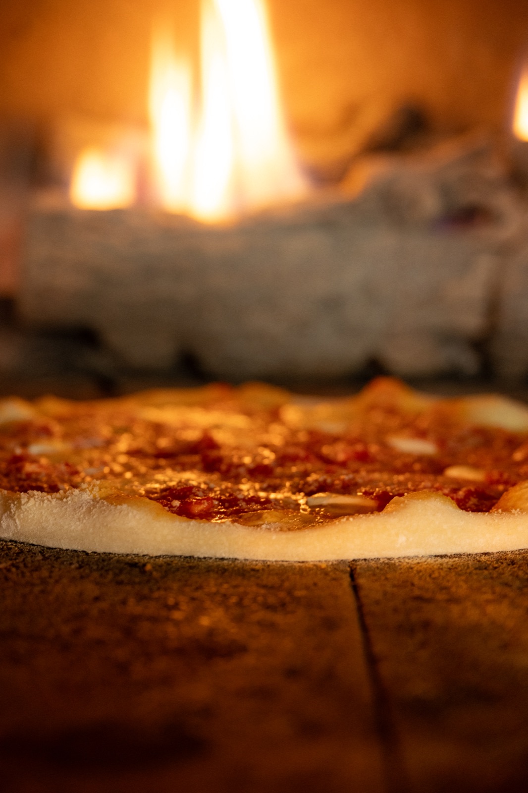 Pizza baking beside the flames in the oven
